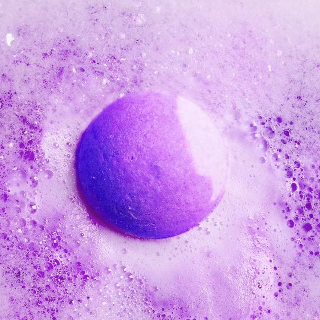 Bubble T Cosmetics blueberry bath bomb. Image shows the bath bomb in water surrounded by lovely purple-coloured water and bubbles. Vegan and cruelty-free. Available at Lovethical along with plenty of other vegan and cruelty-free beauty products, makeup, make up, toiletries and cosmetics for all your gift and present needs.