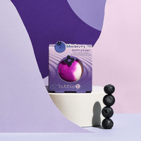 Bubble T Cosmetics blueberry bath bomb. Image shows the bath bomb in its packaging and surrounded by blueberries. Vegan and cruelty-free. Available at Lovethical along with plenty of other vegan and cruelty-free beauty products, makeup, make up, toiletries and cosmetics for all your gift and present needs.