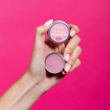 Load image into Gallery viewer, Pura Cosmetics pink tinted lip balm. Vegan and cruelty-free. Image shows a person holding the tin open and showing the vibrant pink colour within. Available at Lovethical along with plenty of other vegan and cruelty-free beauty products, makeup, make up, toiletries and cosmetics for all your gift and present needs. 
