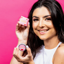 Load image into Gallery viewer, Pura Cosmetics pink tinted lip balm. Vegan and cruelty-free. Image shows a smiling person holding the lip balm with it&#39;s outer carboard packaging. Available at Lovethical along with plenty of other vegan and cruelty-free beauty products, makeup, make up, toiletries and cosmetics for all your gift and present needs. 
