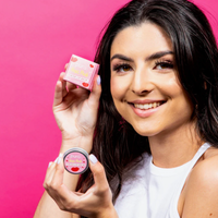 Pura Cosmetics pink tinted lip balm. Vegan and cruelty-free. Image shows a smiling person holding the lip balm with it's outer carboard packaging. Available at Lovethical along with plenty of other vegan and cruelty-free beauty products, makeup, make up, toiletries and cosmetics for all your gift and present needs. 