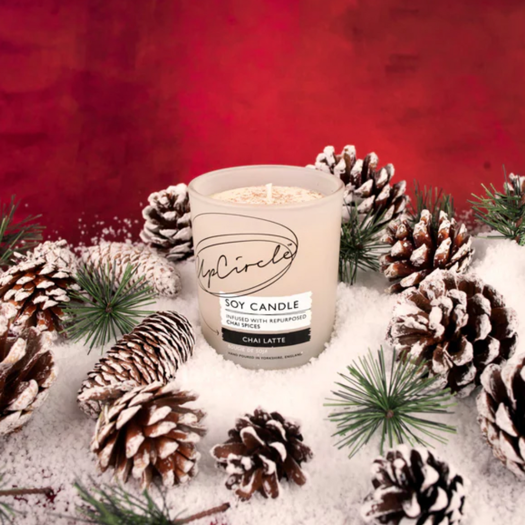 UpCircle chai latte soy wax candle. Vegan and cruelty-free. Image shows the candle surrounded by Christmas pine cones and snow.