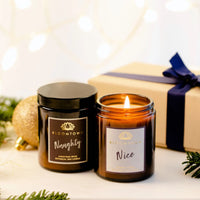 Bloomtown Christmas nice and naughty candle duo gift set - Christmas spice and almond and rose. Vegan and cruelty-free. Image shows one lit candle, one un-lit candle and a lovely gift box with a blue bow on it. Available at Lovethical along with plenty of other vegan and cruelty-free beauty products, makeup, make up, toiletries and cosmetics for all your gift and present needs. 