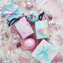 Load image into Gallery viewer, Miss Patisserie joy bath ball. Image shows the box, the unboxed bath ball, some wrapped presents, the Peace bath ball and lots of Christmas decorations such as tinsel. Vegan and cruelty-free. Available at Lovethical along with plenty of other vegan and cruelty-free beauty products, makeup, make up, toiletries and cosmetics for all your gift and present needs. 
